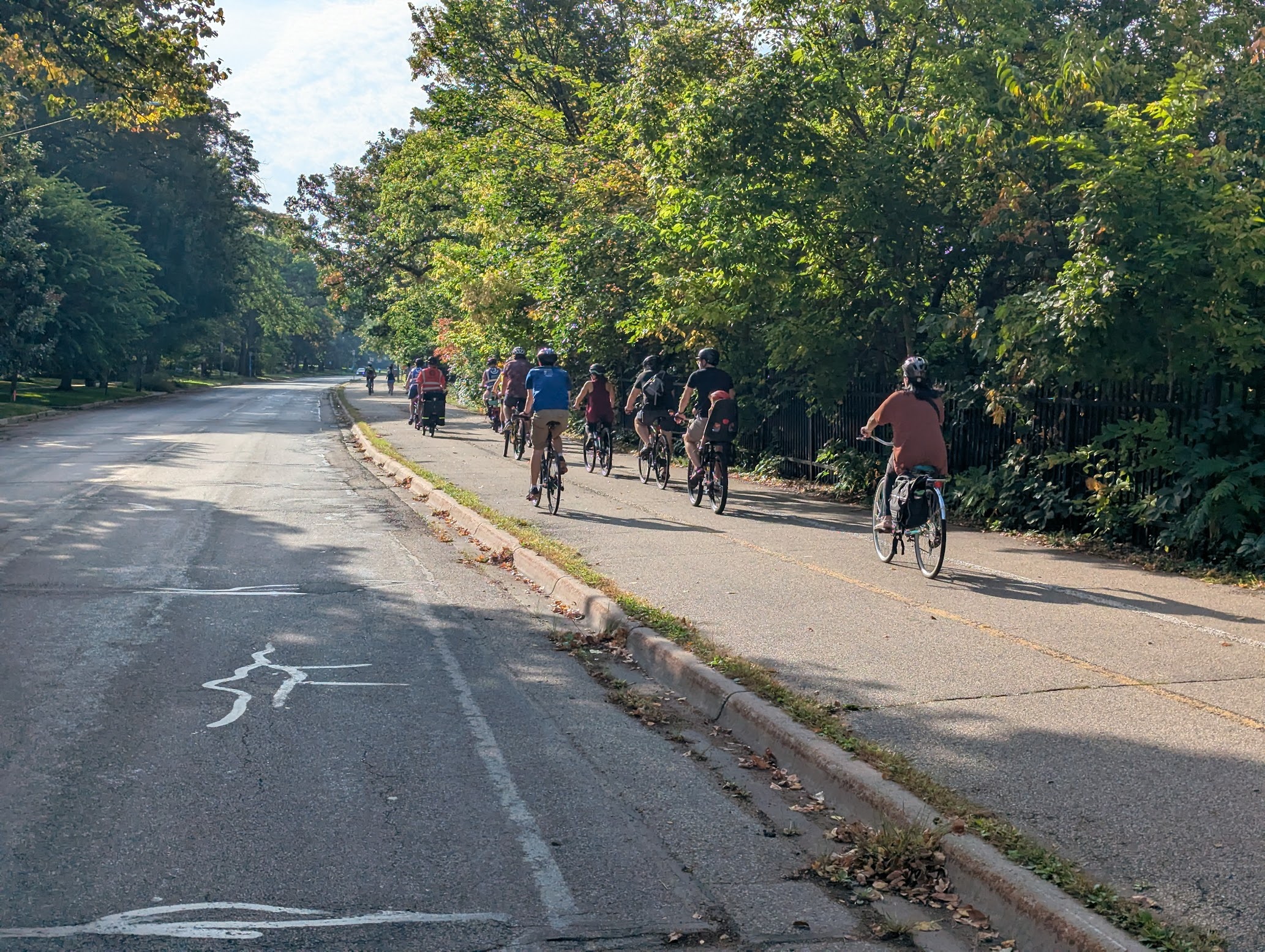 A group of families ride on an off street protected trail alongside trees.