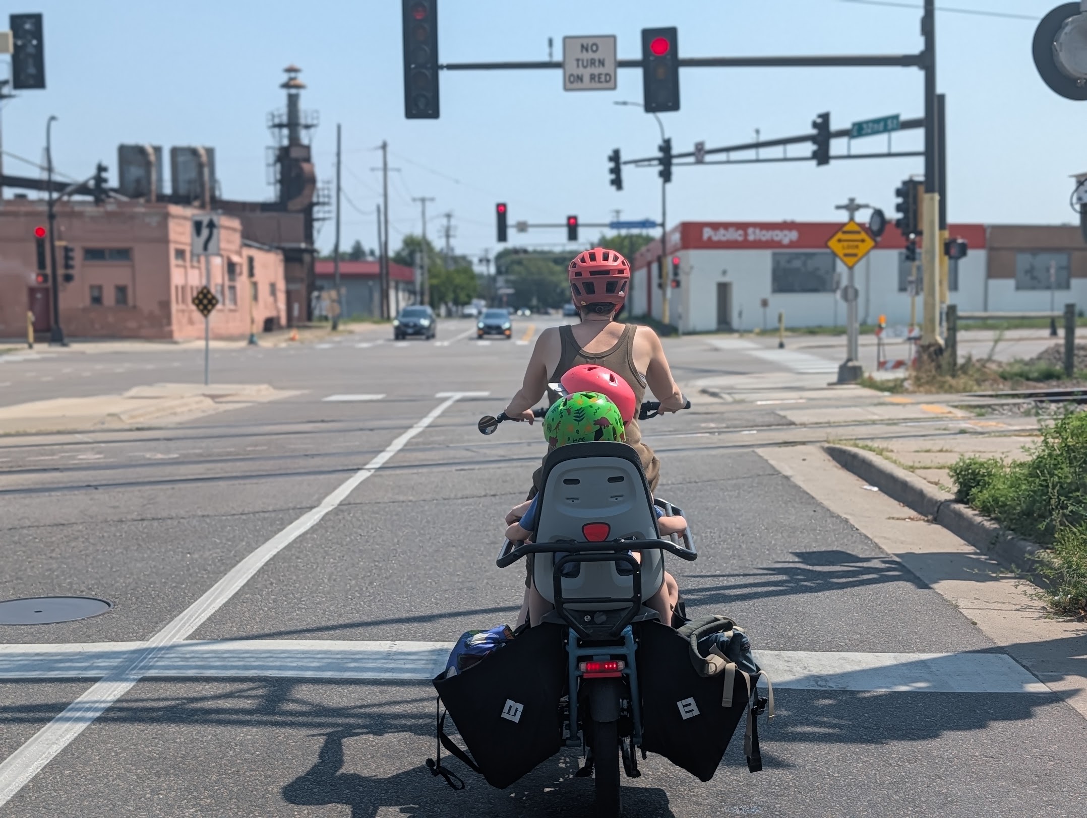 A parent on an e-cargo bike with two kiddo's onboard prepares to cross a wide road.