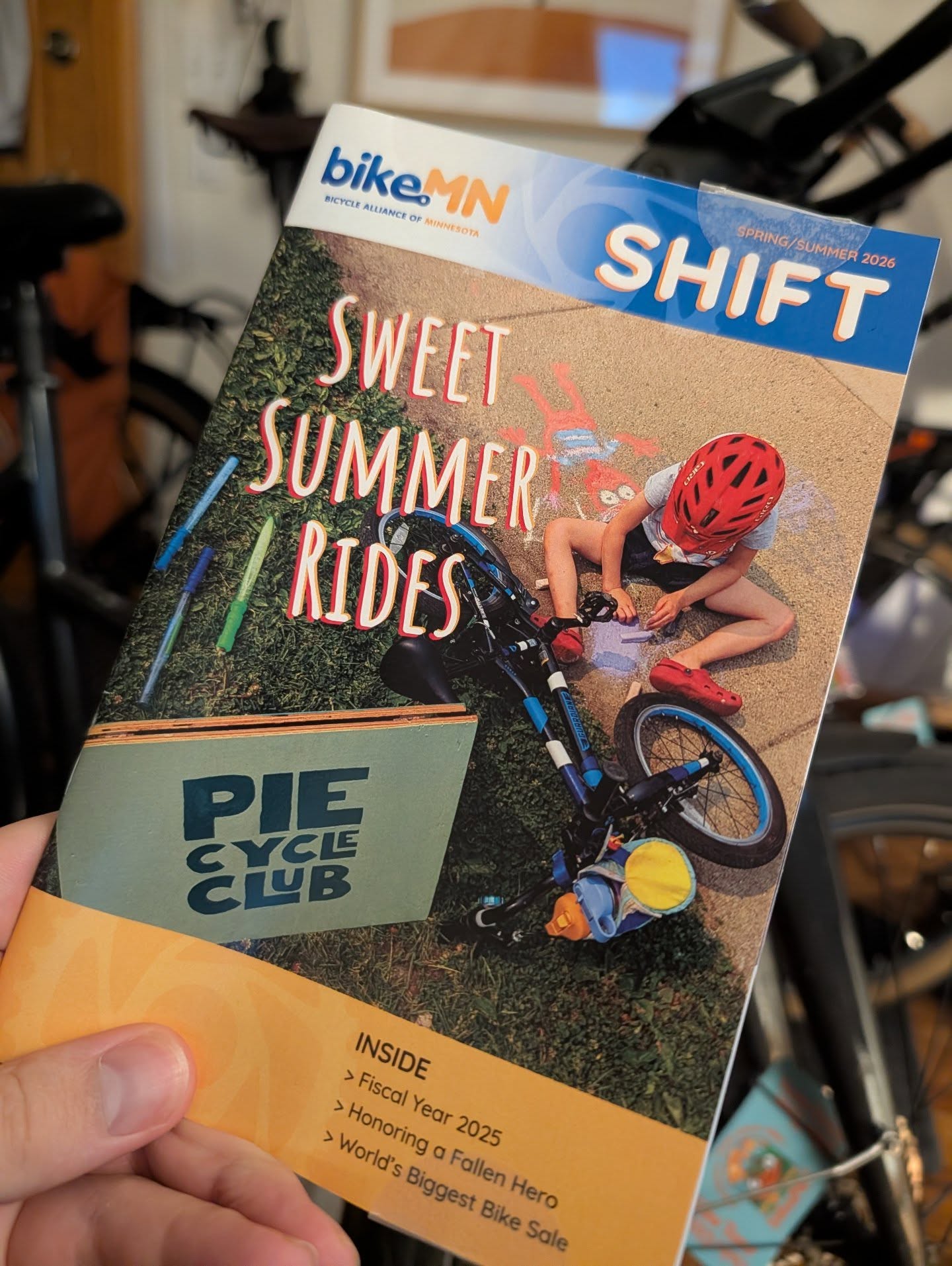 photo of the latest edition of shift. a child sits on the ground playing with chalk next to a bicycle